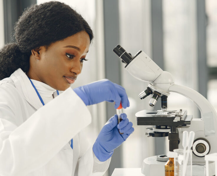 Medical doctor girl working with a microscope. Young female scientist doing vaccine research.